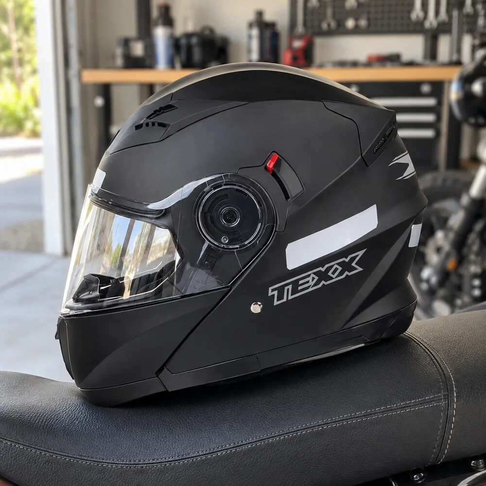 Capacete articulado preto fosco com viseira transparente, sobre o banco de uma moto numa garagem iluminada
